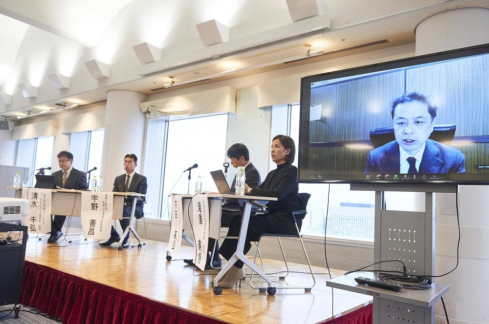 画像：パネル討論中の壇上の様子。左から、清水教授、宇野氏、内田氏、滝澤教授の順に席についている。滝澤教授の左に、祝迫教授が映ったモニターが配置されている。